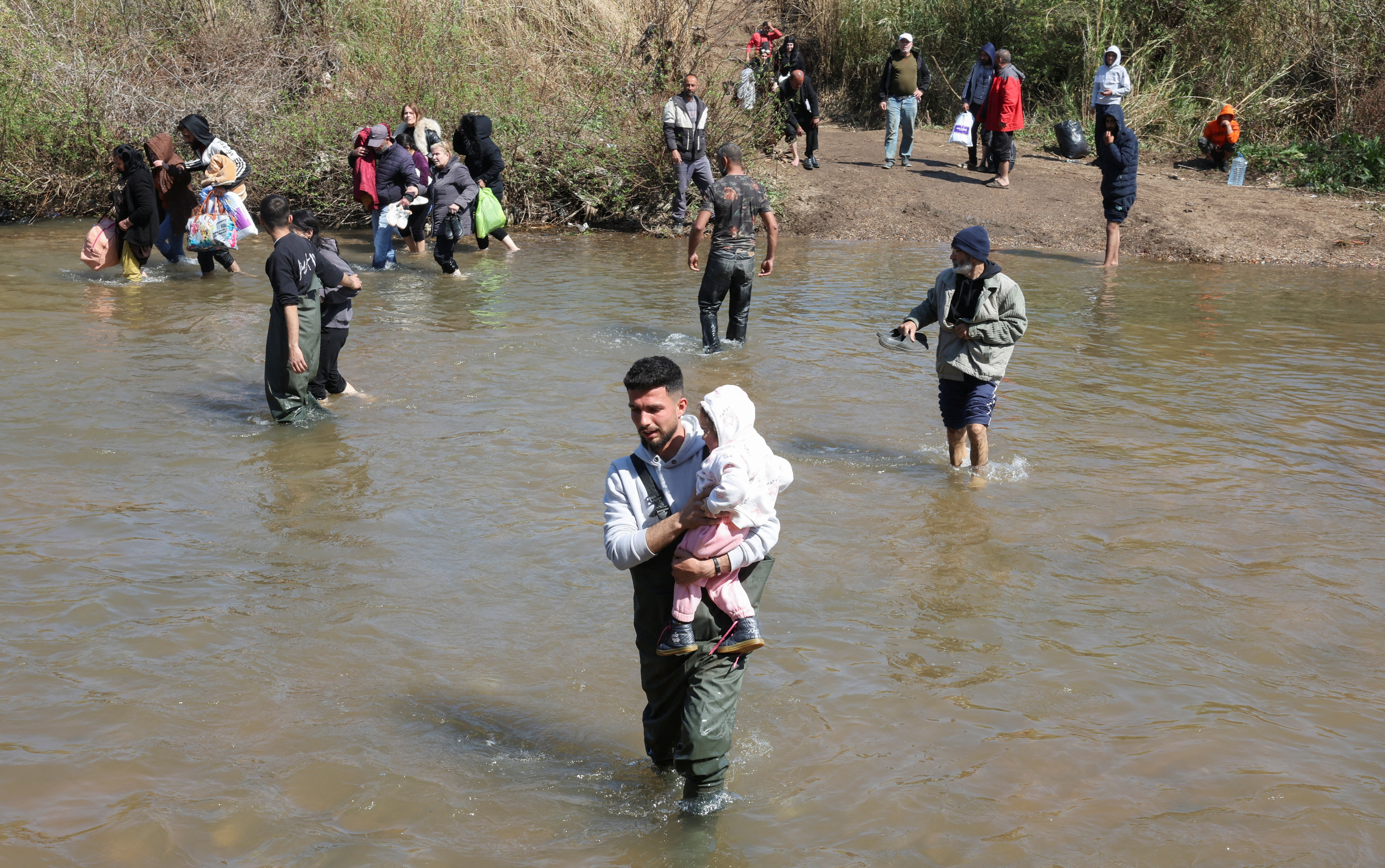 Alawite Syrians, who fled the violence in western Syria, walk in Nahr El Kabir River, after the reported mass killings of Alawite minority members, in Akkar, Lebanon March 11, 2025. REUTERS/Mohamed Azakir