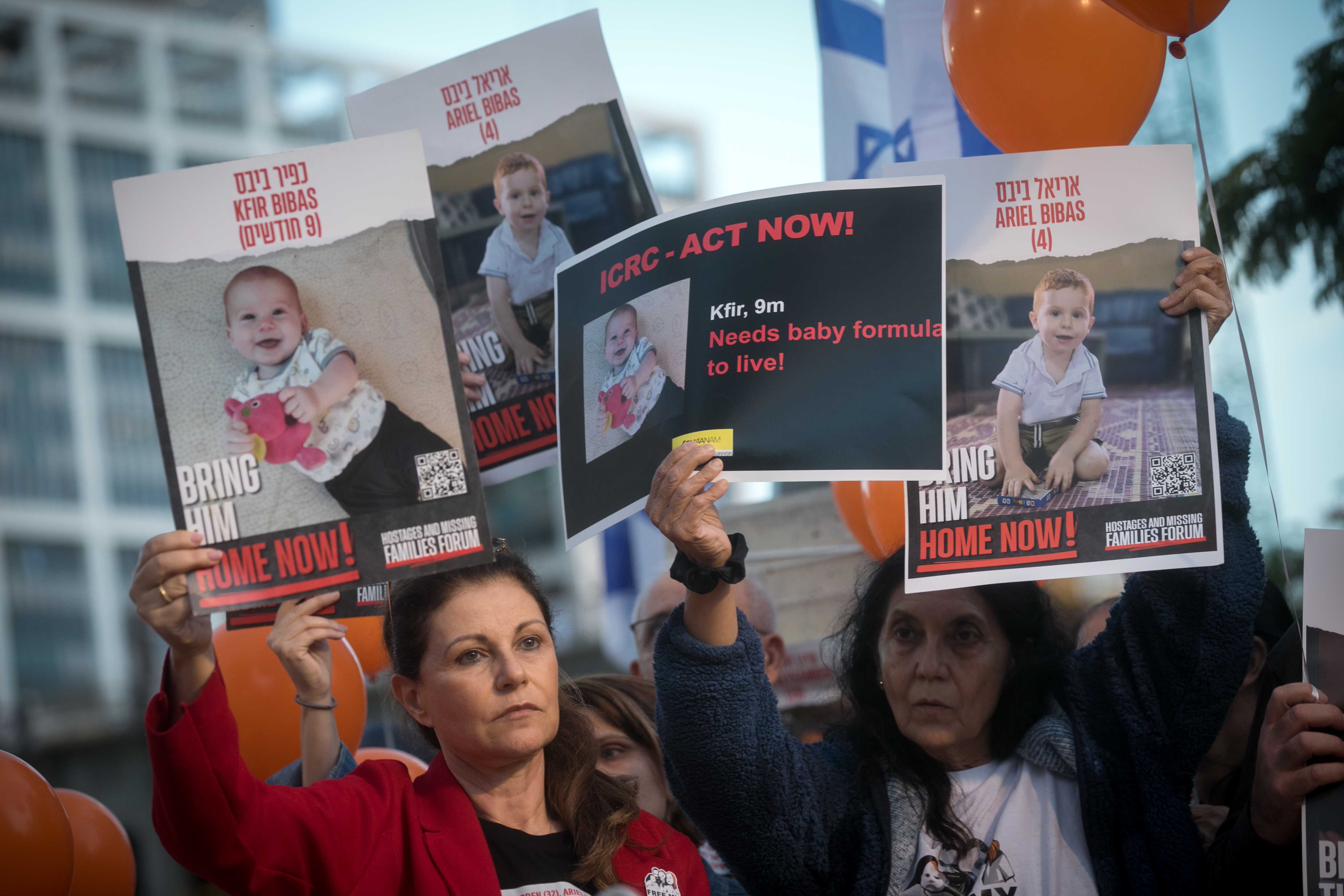 Israelis hold photographs of the Bibas family, and orange balloons, at a press conference calling for the release of 10 month old Kfir, 4 year old Ariel, and their parents Shiri and Yarden Bibas. at 